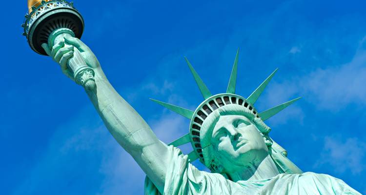 Close-up upward view of the Statue of Liberty's torch and crown against a deep blue sky.