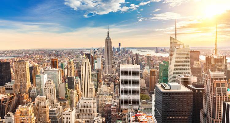 Sweeping aerial skyline of Manhattan with the Empire State Building under a glowing late-day sun.