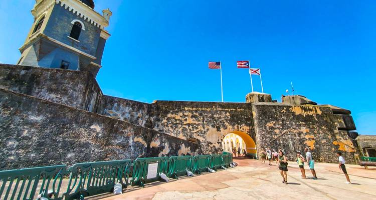 Visitantes caminando alrededor de una fortaleza histórica con una torre y banderas.