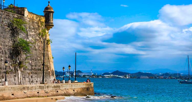 Fuerte histórico junto al océano con personas sentadas a lo largo del muro.