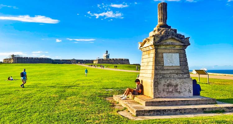 Personas sentadas en el césped frente a un fuerte histórico.