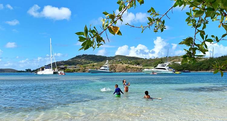 Niños jugando en aguas poco profundas con barcos a lo lejos.