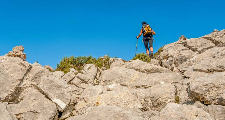 Personne faisant de la randonnée sur un terrain rocheux sous un ciel bleu dégagé.