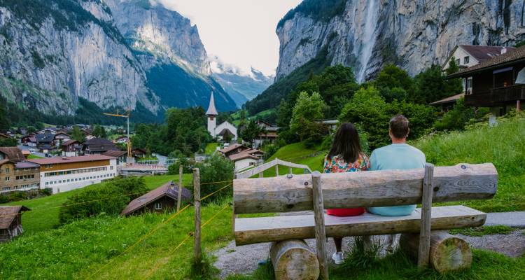 Couple sitting on a bench overlooking a scenic valley and church.