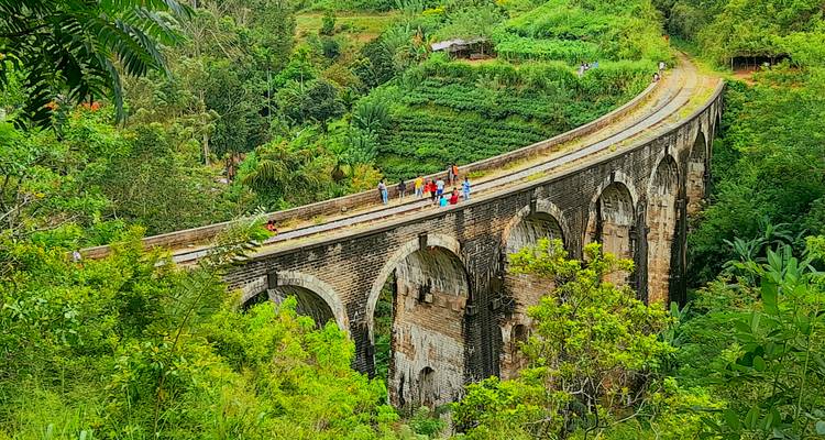 Lush green valley frames Sri Lanka's iconic Nine Arches Bridge with travellers walking along the railway.