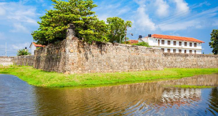 Un mur de fort en pierre et un bastion se reflètent dans un fossé calme sous un ciel dégagé.