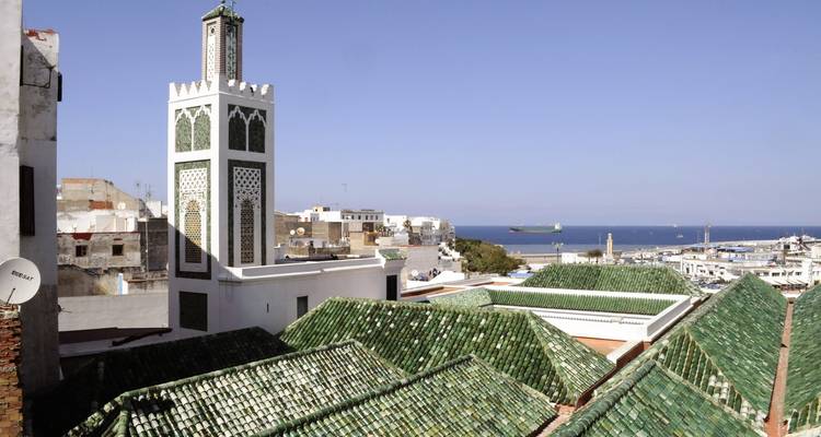 Blick auf ein Moscheeminarett und Dächer mit dem Meer im Hintergrund.