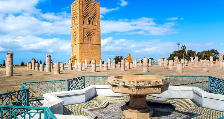 A historic site with a tower and scattered columns under a blue sky.