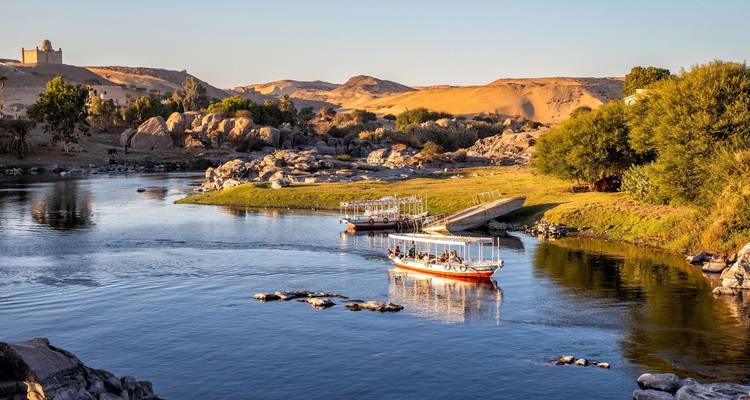 Flusslandschaft mit Booten, Bäumen und fernen Wüstenhügeln