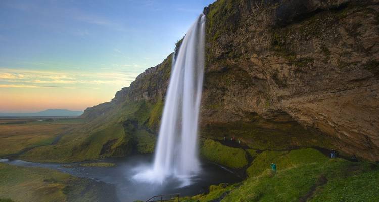 Cascada Seljalandsfoss con exuberante vegetación verde al atardecer.