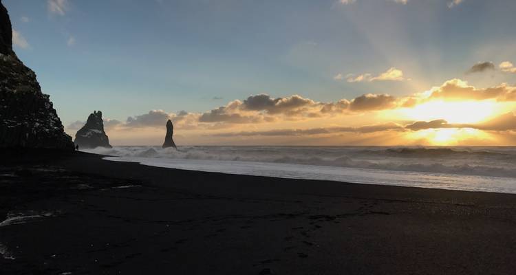 Playa de arena negra con olas del océano y farallones durante la puesta de sol.
