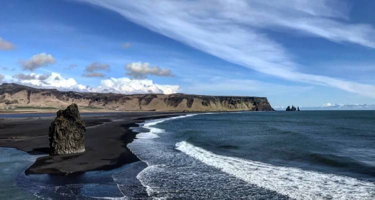 Vista panorámica de una playa de arena negra con acantilados distantes.