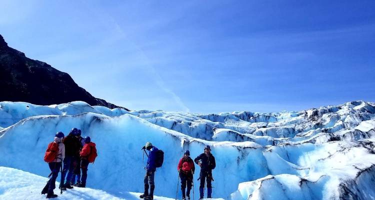 Group of people standing on a glacier with blue sky above.