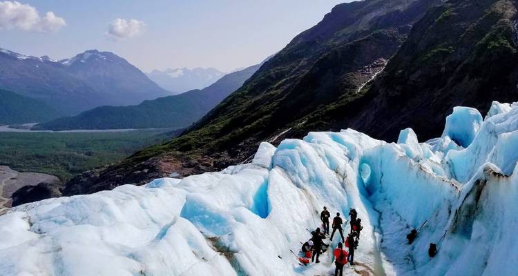 Hikers navigating through a glacier with mountains in the background.