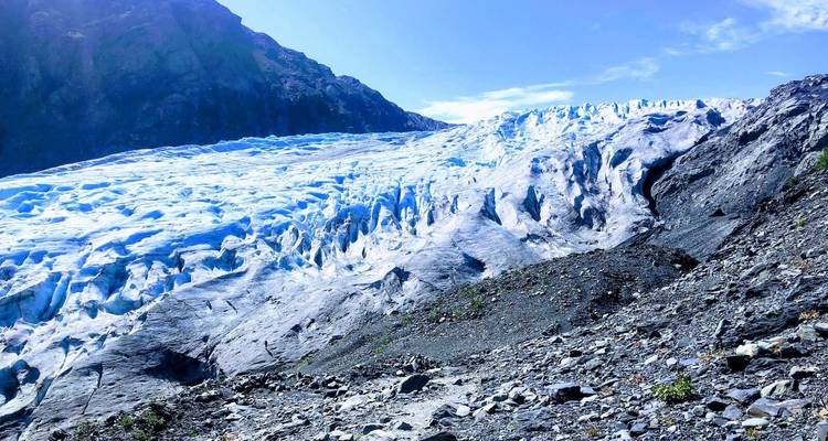 Expansive glacier surface with clear blue ice and rugged mountains.