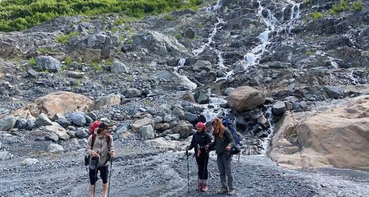 People standing near a rocky waterfall in a mountainous area.