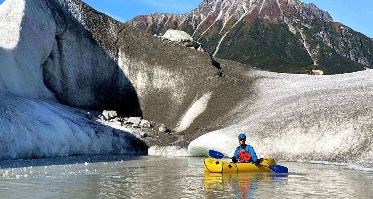 Person kayaking amidst striking glacial landscapes.