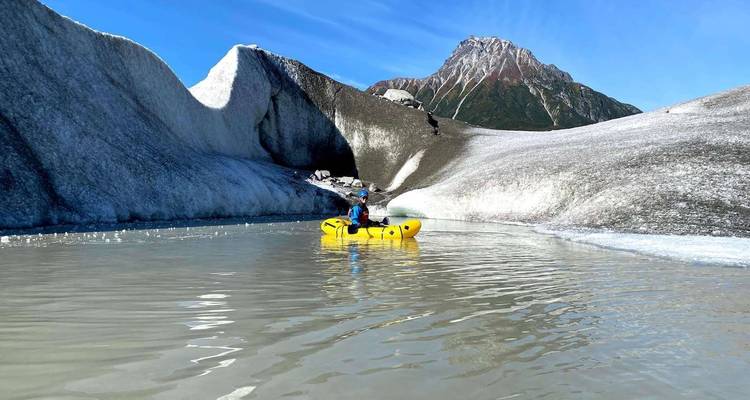 Kayaker exploring icy waters below a glacier.