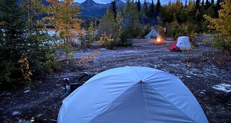 Camping site at dusk with tents near a forest and mountains.