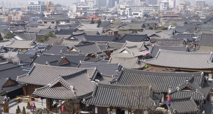 Dichte groep van traditionele grijze dakpannen van hanok-huizen die zich uitstrekken over het Jeonju Hanok Village met moderne stad daarachter.