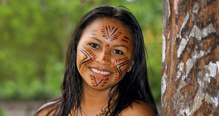 Une femme avec des peintures faciales traditionnelles appuyée contre un arbre.