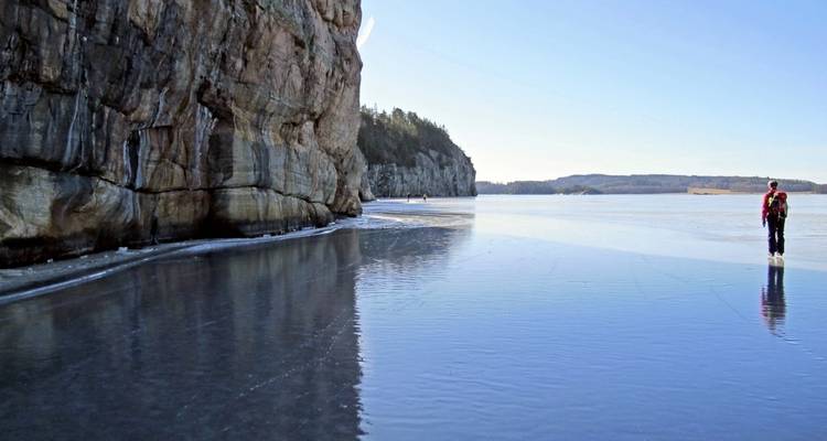 Person ice skating on a frozen lake near a cliff.