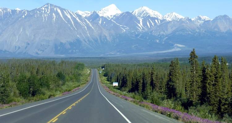 Long straight road leading towards snow-capped mountains.