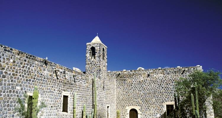 Stone building with a bell tower and cacti in front.
