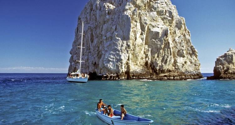 Boats near a large rock formation in clear blue water.