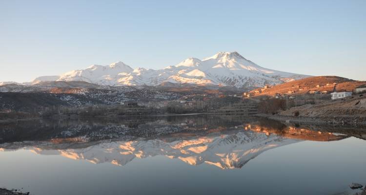 Montañas cubiertas de nieve reflejadas en un lago al amanecer.