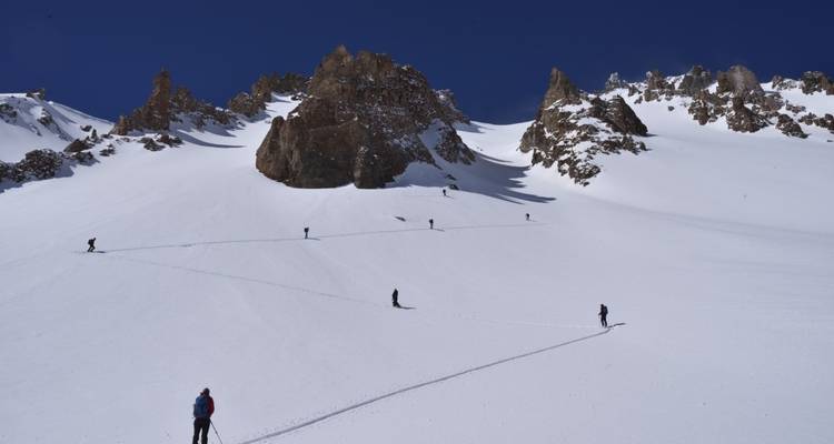 Esquiadores caminando en un terreno nevado con picos rocosos.
