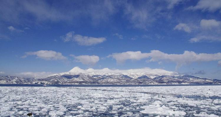 Montagnes enneigées avec un lac de glace partiellement couvert en contrebas.