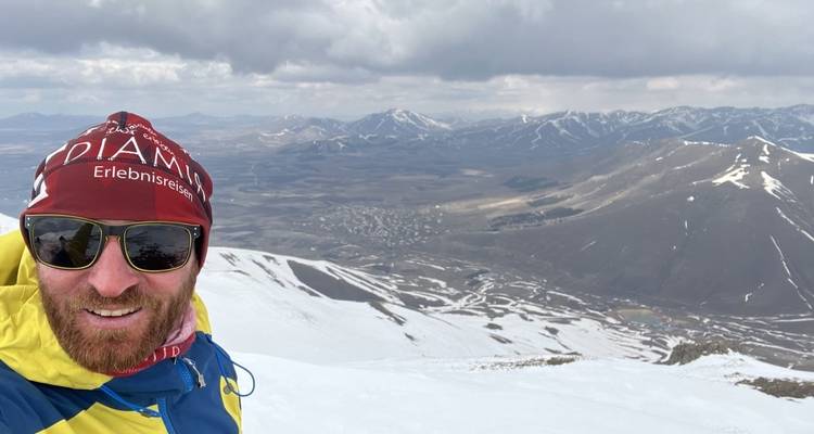 Person taking a selfie on a snow-covered mountain, with a view of the valley.