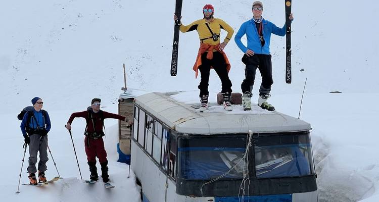 Group of skiers standing on a bus covered in snow.