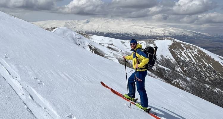A skier on a snowy slope with a mountain in the background.