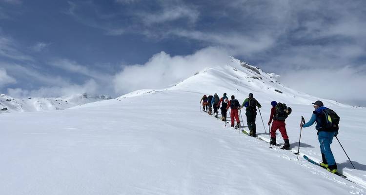 Group of skiers walking up a snowy trail toward a mountain peak.