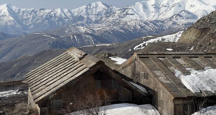 Two snow-covered rustic rooftops with majestic mountains in the background.