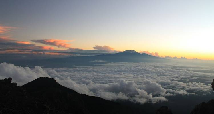 Un pico de montaña al amanecer con nubes abajo.