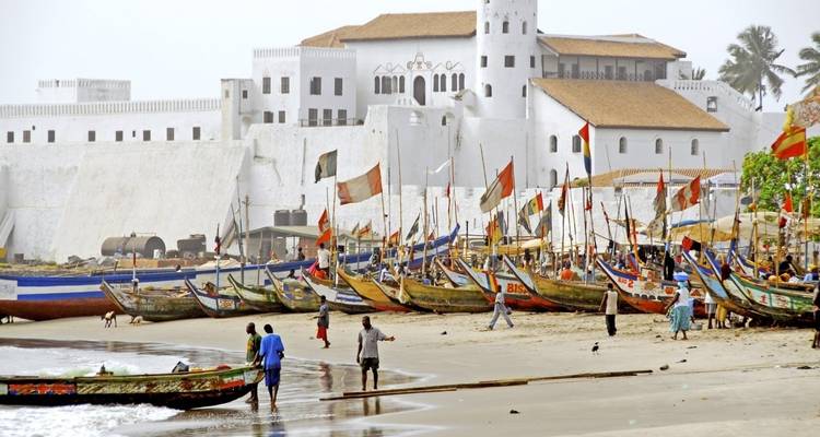 Des bateaux de pêche sur une plage près d'un bâtiment historique blanc.