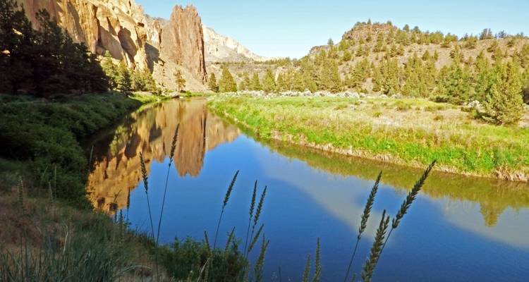Felsige Klippen spiegeln sich in einem gewundenen Fluss durch eine grüne Landschaft.