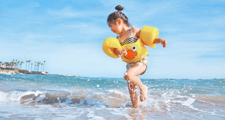 A young child playing in the ocean surf, wearing inflatable armbands.
