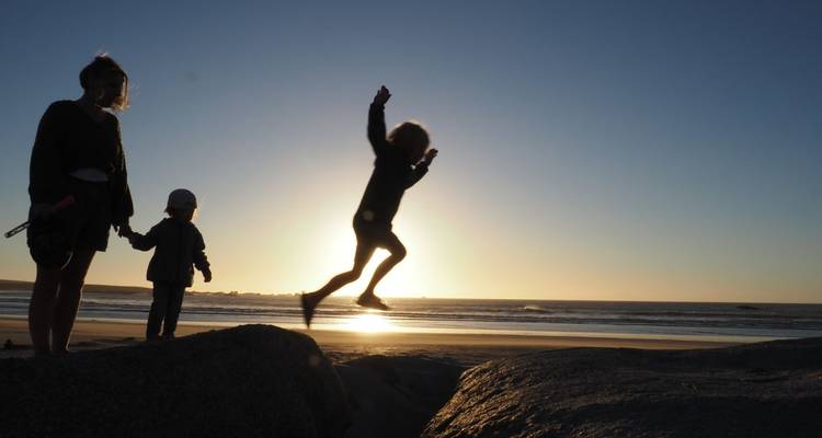 Silhouette of a child leaping on a beach at sunset.