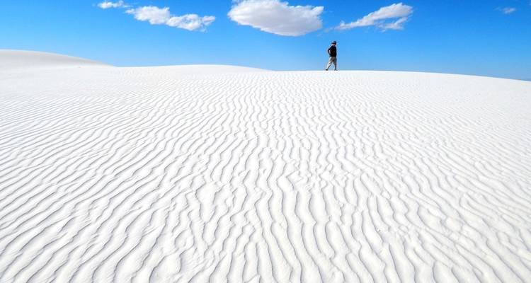 Persoon wandelend op het uitgestrekte witte zand onder een blauwe hemel.