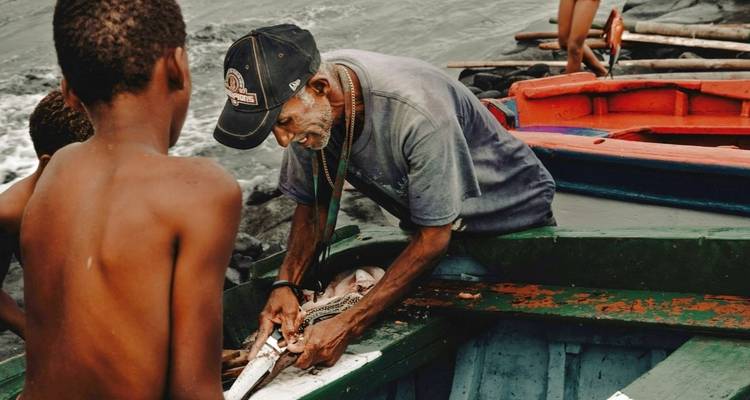 Pêcheur nettoyant du poisson sur un bateau avec de jeunes garçons qui observent.