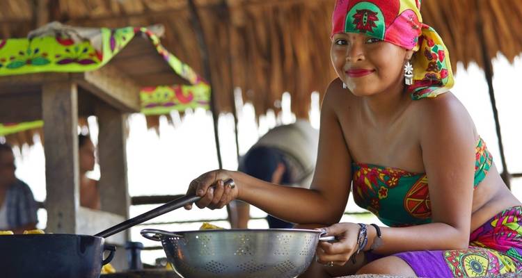 Woman in traditional dress preparing food under a thatched roof.