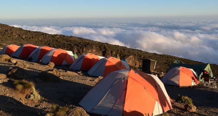 Camping tents set up on a mountainside above the clouds.