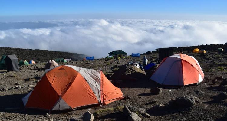 Mountain campsite with tents and cloud cover below.