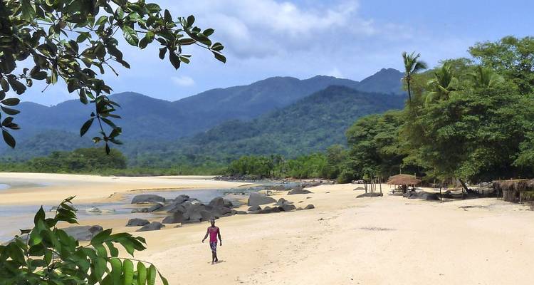 Person, die an einem verlassenen Strand mit Bergen im Hintergrund spaziert.