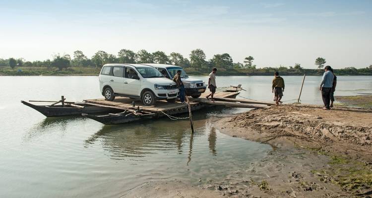 Fahrzeuge, die auf einem handgefertigten Floß über einen Fluss transportiert werden.