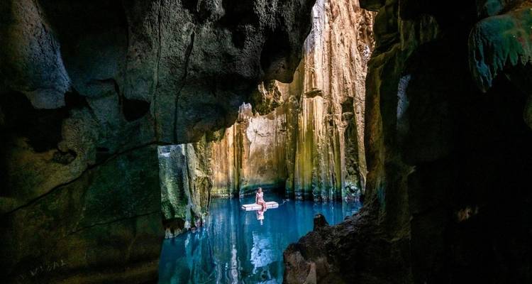 Person floating in a sunlit cave pool.